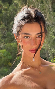Woman with a messy bun and freckles wearing gold jewelry outdoors
