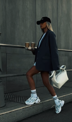 Woman in a black cap and oversized blazer holding coffee cups outdoors