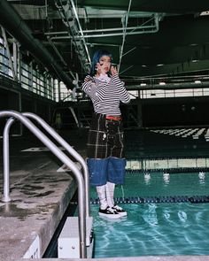 Person with blue hair and striped shirt standing in an indoor pool