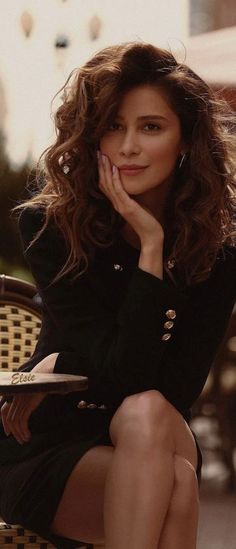 Woman with curly hair in a black blazer at an outdoor cafe