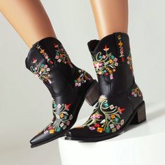 Black cowboy boots with colorful floral embroidery on a white surface