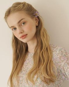 Young woman with blonde hair and a purple flower in her hair, wearing a floral top