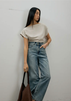 Woman with long black hair wearing a beige top and wide leg jeans