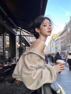 Woman in an off-shoulder top holding a coffee cup on a city street