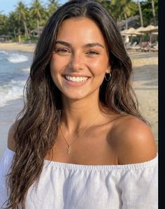 Woman with long hair and an off-shoulder top smiling on a beach