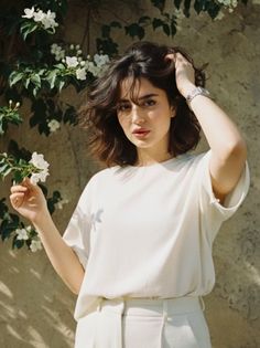 Woman with short hair in a white t-shirt and pants holding white flowers outdoors