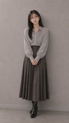 Woman with long hair and glasses wearing a long sleeve shirt and pleated skirt