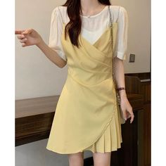 Woman in a yellow dress over a white shirt, holding a shoulder bag indoors