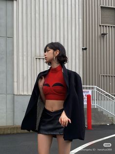 Woman in a red crop top and black mini skirt with a blazer over her shoulders
