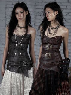 Two women in steampunk-inspired leather corsets and long skirts against a white brick wall