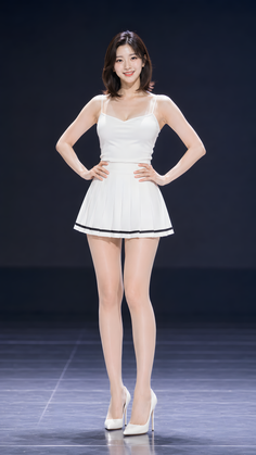 Woman in a white top and pleated skirt posing indoors with a dark background