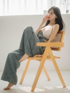 Woman in denim overalls and a white bra sitting on a wooden chair