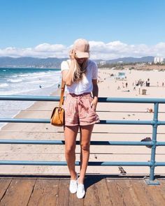 Woman in pink shorts and a white t-shirt on a pier overlooking a beach