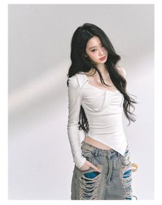 Woman with long black hair wearing a white top and ripped jeans indoors