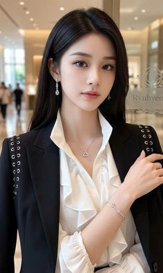 Woman with long black hair wearing a black blazer and white ruffled shirt indoors