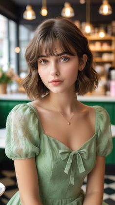 Woman with short brown hair wearing a green dress with a bow detail indoors