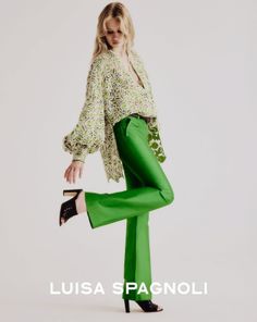 Woman with blonde hair wearing green pants and a lace top in a studio