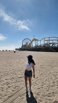 Woman in a denim skirt and crop top on a beach with an amusement park in the background