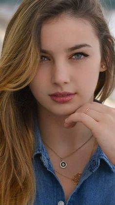 Woman with long hair and blue eyes wearing a denim shirt and layered necklaces