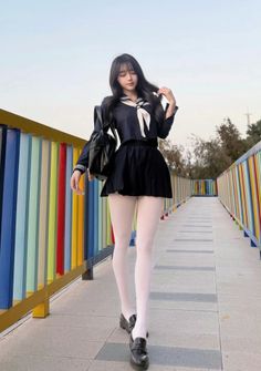 Woman in a school uniform and white tights walking on a bridge with a colorful railing