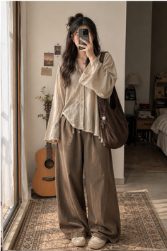 Woman in a loose shirt and wide leg pants taking a mirror selfie indoors