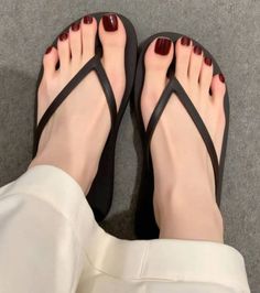 Person wearing black flip flops with red nail polish and white pants