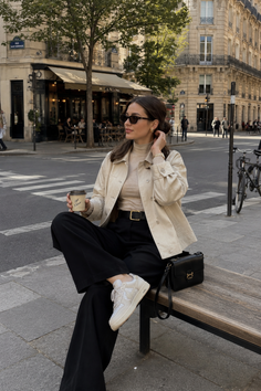 Woman in sunglasses and a beige jacket sitting on a bench on a city street