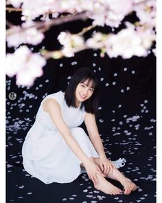 Woman in a white dress sitting on a black surface with cherry blossoms and petals