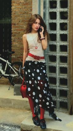 Woman with long hair wearing a polka dot skirt and red tights, talking on a phone