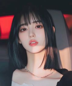 Woman with short black hair and bangs wearing a necklace, with warm lighting