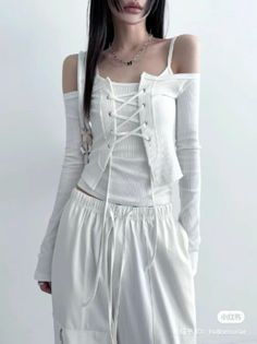 Person with long black hair wearing a white lace-up top and white pants indoors