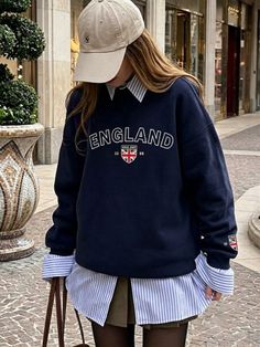 Person wearing a navy sweatshirt and baseball cap over a striped shirt outdoors