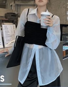 Person in a sheer light blue shirt and black top holding a coffee cup indoors