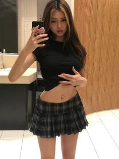 Woman in a black cropped top and plaid skirt taking a mirror selfie
