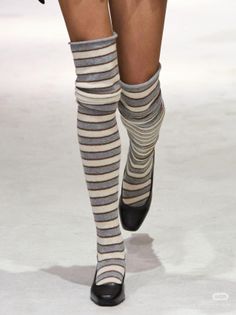 Person wearing striped knee-high socks and black shoes walking on a white surface