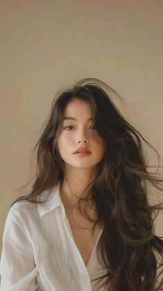 Woman with long brown hair wearing a white shirt, looking directly at the camera