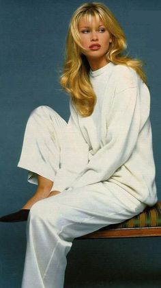 Woman with long blonde hair wearing a white sweater and pants, sitting on a bench