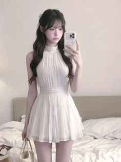 Woman in a white dress taking a mirror selfie in a bedroom