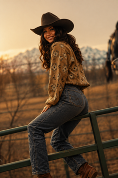 Woman in a cowboy hat and jeans sitting on a fence at golden hour