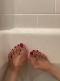Feet with red nail polish soaking in a bathtub