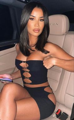 Woman with black hair wearing a black cutout top and skirt in a car
