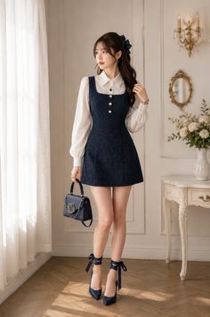 Woman in a navy mini dress and white shirt holding a handbag indoors