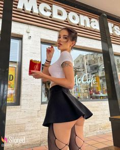 Woman in a short skirt and fishnet stockings holding fries outside a McDonald's