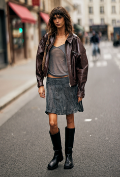 Woman in a brown leather jacket, sheer top, and mini skirt on a street