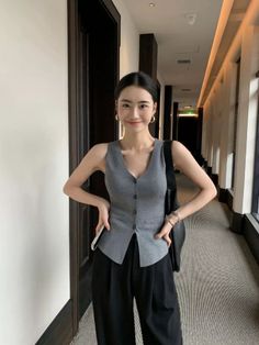 Woman in a gray vest and black pants smiling in an indoor hallway