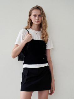 Woman with blonde hair wearing a black top over a white t-shirt and a black skirt