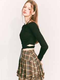 Woman in a black long sleeve top and plaid skirt posing in a studio