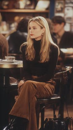 Blonde woman in a black turtleneck and brown pants sitting indoors