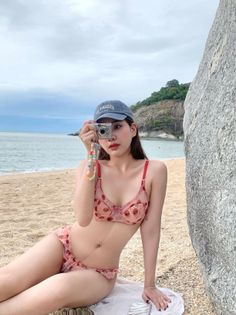 Woman in a pink bikini and baseball cap holding a camera on a beach