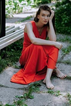 Woman in a red dress sitting barefoot on the ground outdoors
